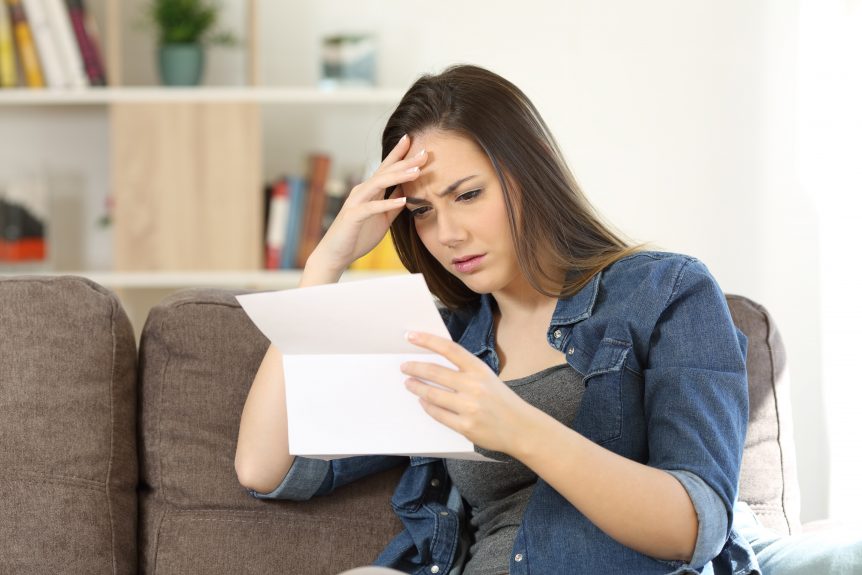 Concerned woman reading bad news in a letter sitting on a couch in the living room at home